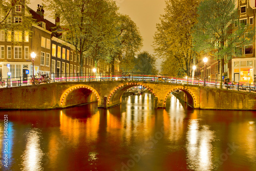 Picturesque Night View of Amterdam Cityscape with One The Canals Along  With Illuminated Bridge and Traditional Dutch Houses At Twilight on Background