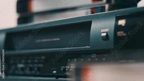 Insert VHS cassette into VCR player. Black vintage videotape cassette recorder on a desk with many archived video cassettes. Male hand inserting old VHS Tape into a retro player. Home video, nostalgia photo