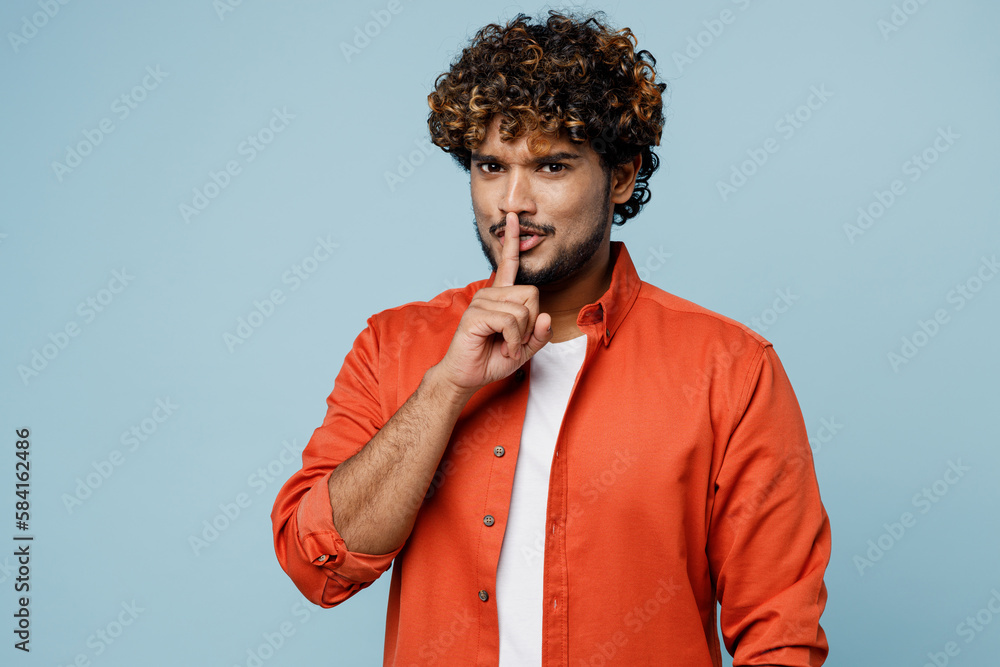 Young secret Indian man wear orange red shirt white t-shirt say hush be quiet with finger on lips shhh gesture isolated on plain pastel light blue cyan background studio portrait. Lifestyle concept. Young secret Indian man wear orange red shirt white t-shirt say hush be quiet with finger on lips shhh gesture isolated on plain pastel light blue cyan background studio portrait. Lifestyle concept.