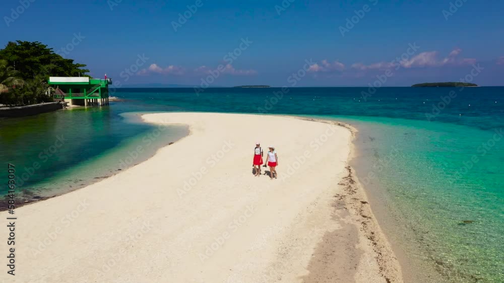 Tourists walk along the white sandy beach. Himokilan Island, Leyte Island, Philippines. Two girls are walking along the beach. White sandy beach with a turquoise lagoon. Summer holiday vacation Tourists walk along the white sandy beach. Himokilan Island, Leyte Island, Philippines. Two girls are walking along the beach. White sandy beach with a turquoise lagoon. Summer holiday vacation