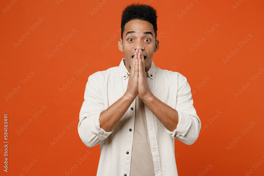 Young surprised shocked happy man of African American ethnicity wear light shirt casual clothes cover mouth with hands look camera isolated on orange red background studio portrait. Lifestyle concept. Young surprised shocked happy man of African American ethnicity wear light shirt casual clothes cover mouth with hands look camera isolated on orange red background studio portrait. Lifestyle concept.