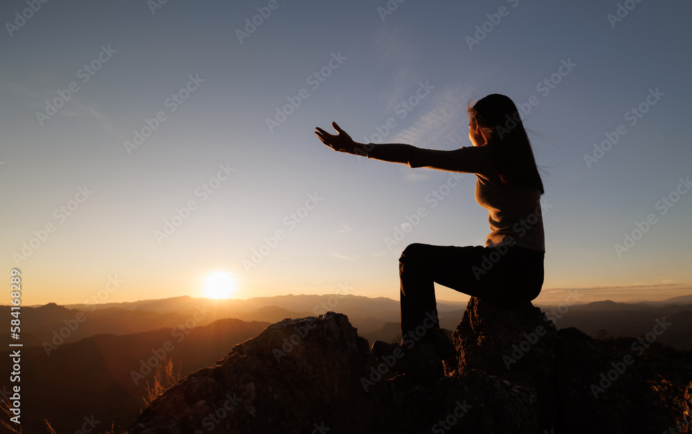 Silhouette of  man rise hand up on top of mountain and sunset sky abstract background. Freedom and travel adventure concept. pray or Praying, remembering God, Copy space .
