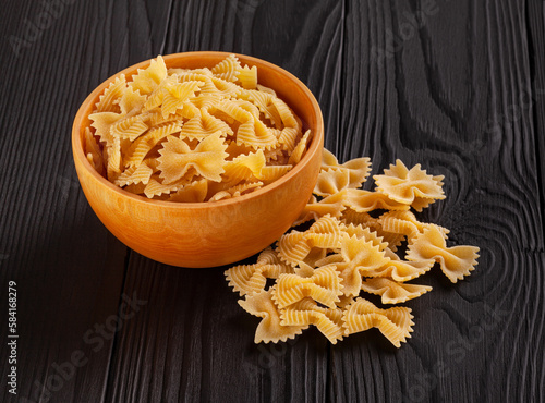 Obraz na płótnie Uncooked farfalle rigate pasta in wooden bowl on black wooden background w salonie