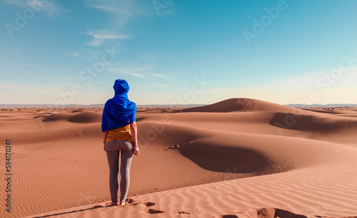 Woman posing with blue turban looking at panorama desert sand dune landscape