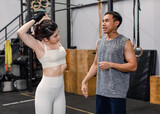 Asian professional muscular male personal trainer teaching female model fit strong body sporty athletic fitness model in sport bra legging standing holding hands arms stretching in CrossFit gym