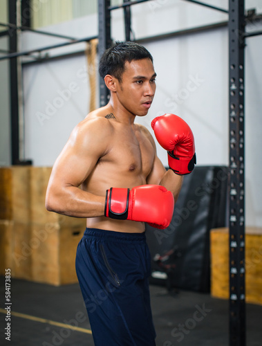 Asian young muscular fit strong body sporty athletic shirtless male fitness model in red boxing gloves with tattoo standing guarding footwork workout exercising sparring training alone in Crossfit gym © Bangkok Click Studio