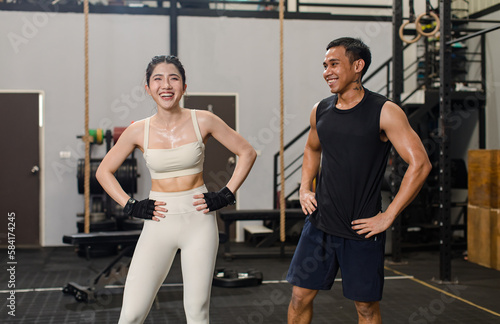 Asian professional male personal trainer take break relax rest talking with young muscular fit strong body sporty athletic sexy female fitness model holding drinking water bottle in Crossfit gym © Bangkok Click Studio