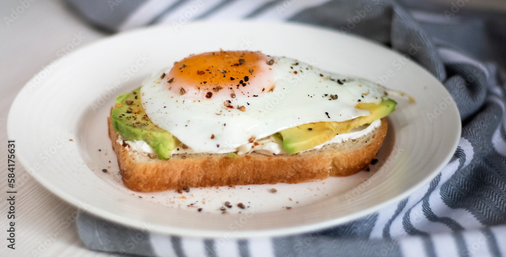 A kind of healthy toast with cream cheese, avocado and fried eggs on toast on a plate close-up A kind of healthy toast with cream cheese, avocado and fried eggs on toast on a plate close-up
