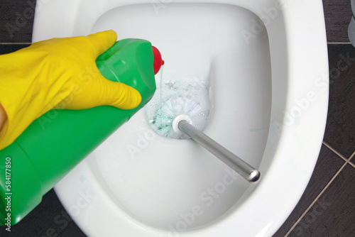 Person in yellow rubber gloves cleans the toilet bowl with a brush and disinfectant photo