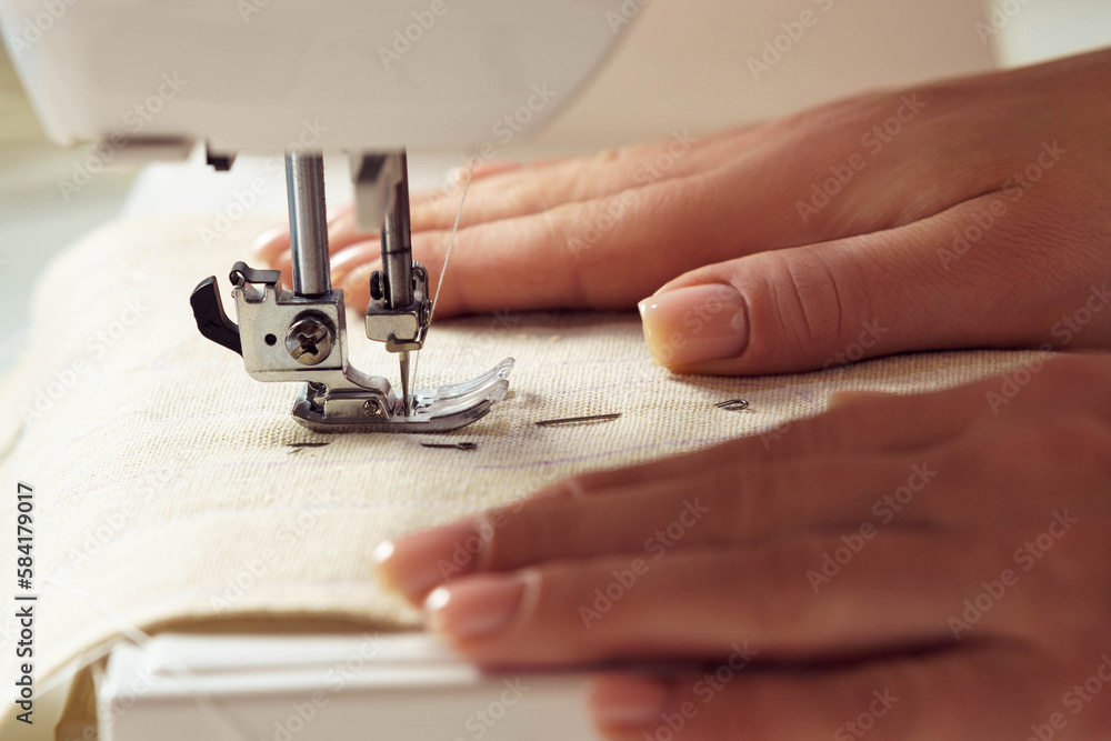 Unrecognizable cropped female dressmaker hands putting white soft fabric textile with stitch contour sewing pattern on sewing machine needle plate under shearer fork. Clothes production in workshop