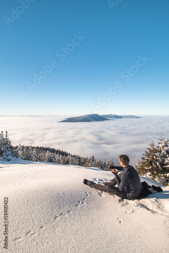 Mountaineer rests on a clearing overlooking the surrounding Beskydy Mountains in the Moravian-Silesian region after climbing Lysa Hora. Enjoying breakfast above the clouds at sunrise