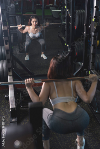 A young and fit woman does barbell squats at the gym. Using the bar weight only.