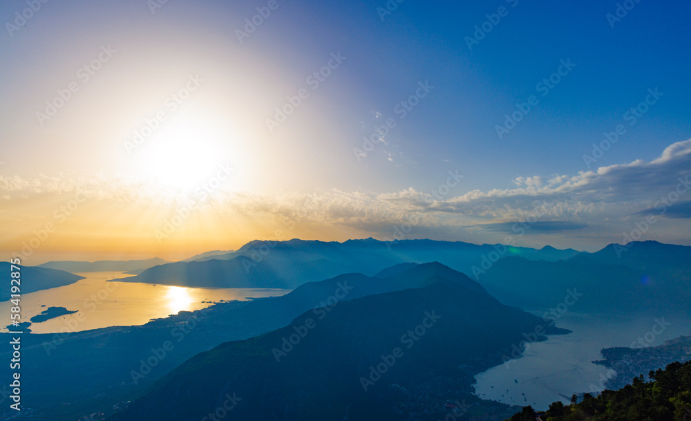 Dazzling sun in the evening sky illuminates all the peaks of the Balkan Montenegrin mountains and the coast of Kotor Bay