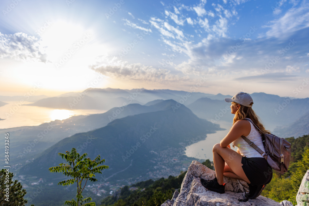 Happy girl with a backpack is on the edge of a high mountain in Montenegro