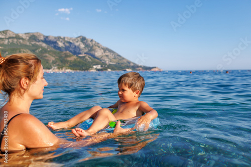 Caring mother rides her son on an inflatable ring in the sea