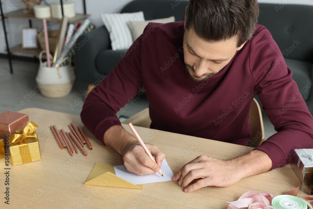 Man writing message in greeting card at wooden table in room Man writing message in greeting card at wooden table in room
