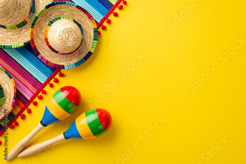 Cinco-de-mayo carnival concept. Top view photo of sombrero hats colorful striped serape and couple of maracas on isolated vivid yellow background with blank space