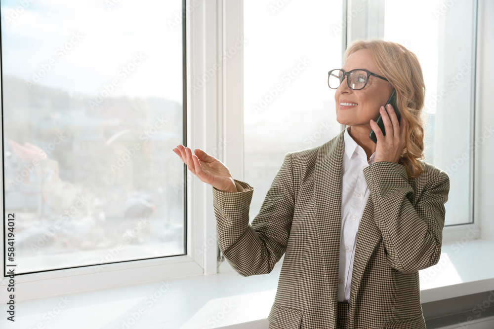 Lady boss talking on smartphone near window indoors, space for text. Successful businesswoman Lady boss talking on smartphone near window indoors, space for text. Successful businesswoman