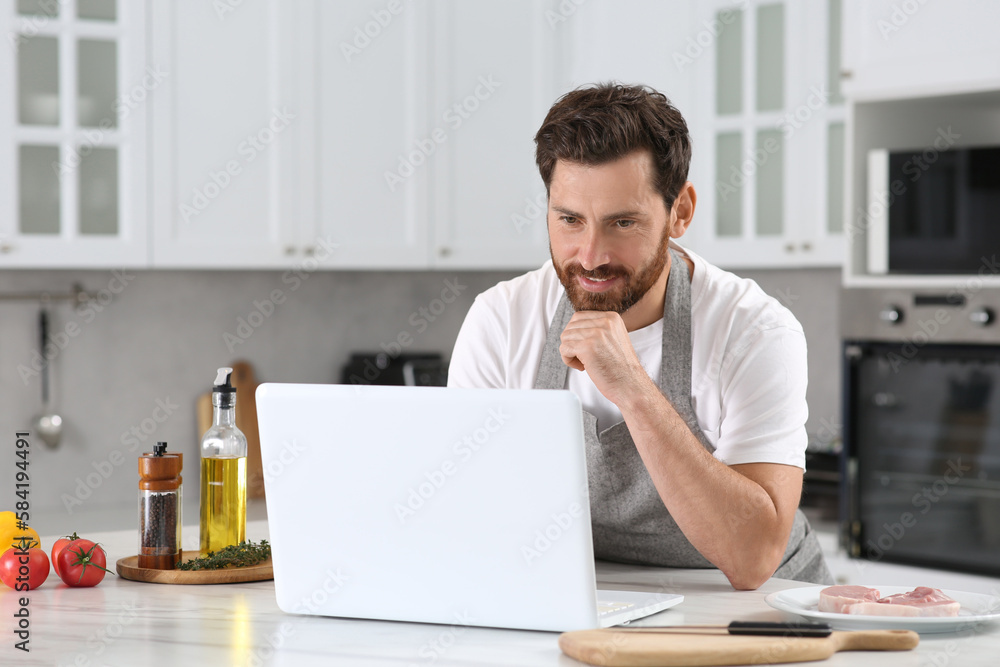 Man making dinner while watching online cooking course via laptop in kitchen