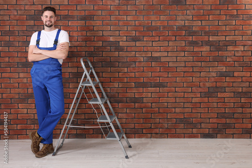 Happy worker near stepladder against brick wall indoors, space for text