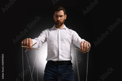 Man in formal outfit pulling strings of puppet on dark background, low angle view