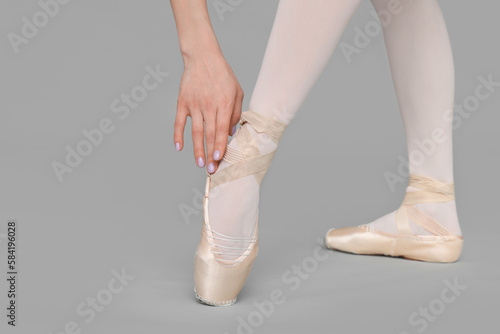 Young ballerina in pointe shoes practicing dance moves on grey background, closeup