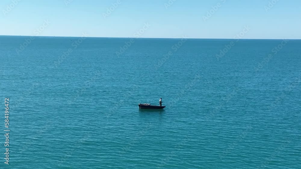Lone person pulls in line while standing on boat in the open ocean Lone person pulls in line while standing on boat in the open ocean