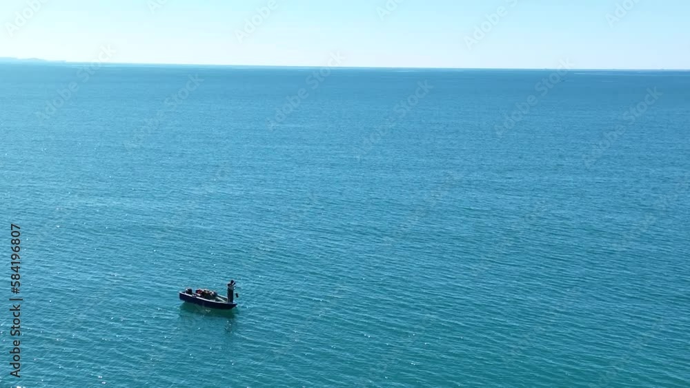 Solo fisherman pulls line up from depths of the ocean on sunny day Solo fisherman pulls line up from depths of the ocean on sunny day