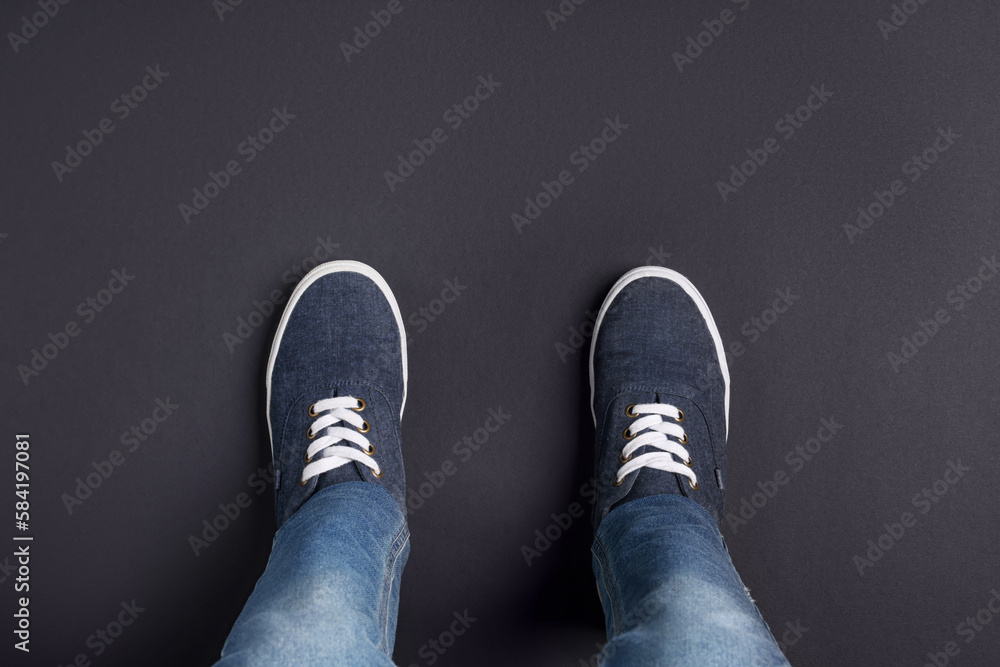 Child in stylish sneakers standing on black background, top view