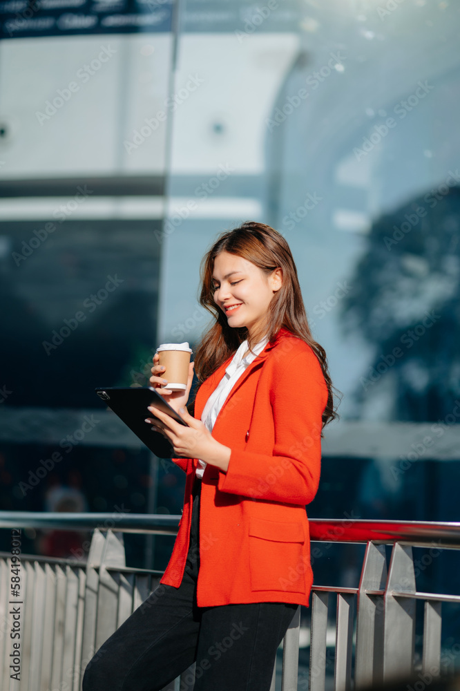 Fototapeta premium Beautiful Asian businesswoman typing laptop computer and digital tablet while holding coffee at office. Office worker at business center.