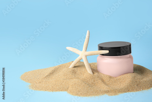 Jar with cream and starfish on sand against light blue background, space for text. Cosmetic product