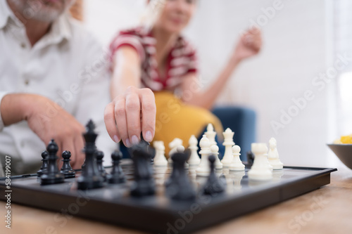 In the living room of the house, an elderly couple sits and relaxes. to begin playing chess together with a chess board with a daughter cheering beside him