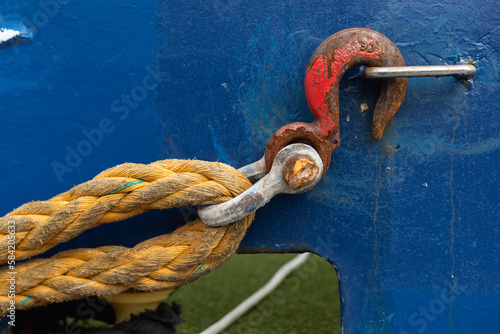 A red hook on a yellow rope hanging from the blue side of the boat.