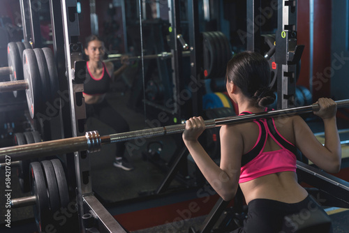 A young woman does barbell squats at the gym. A beginner training her lower body, using the bar weight only.