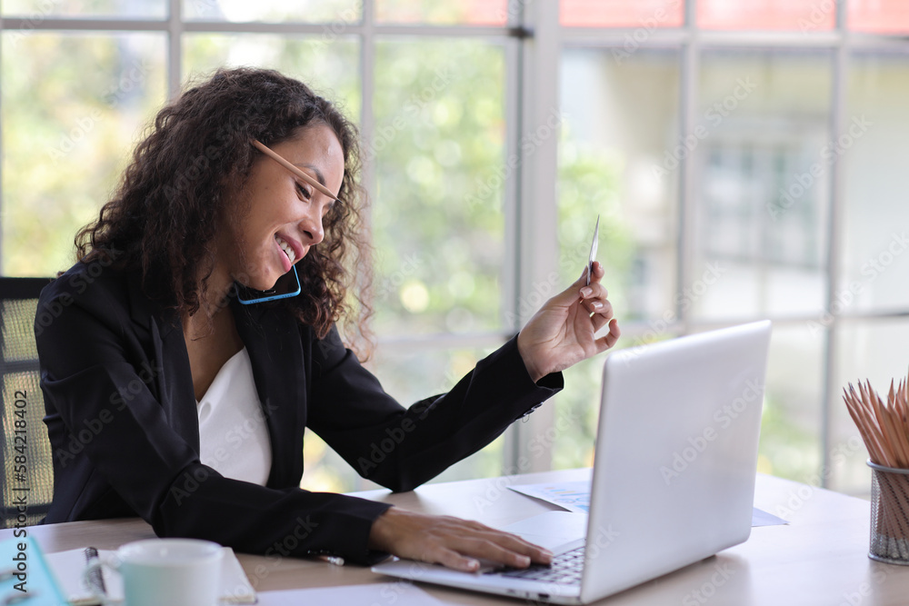 Attractive professional latin female employee worker sitting, using laptop computer with paperwork at home workplace. Businesswoman using speaker phone on smart mobile phone while working. Attractive professional latin female employee worker sitting, using laptop computer with paperwork at home workplace. Businesswoman using speaker phone on smart mobile phone while working.