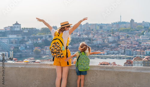 View from behind of Young red-haired mother and little daughter raised thair hands up against the Porto city, Portugal