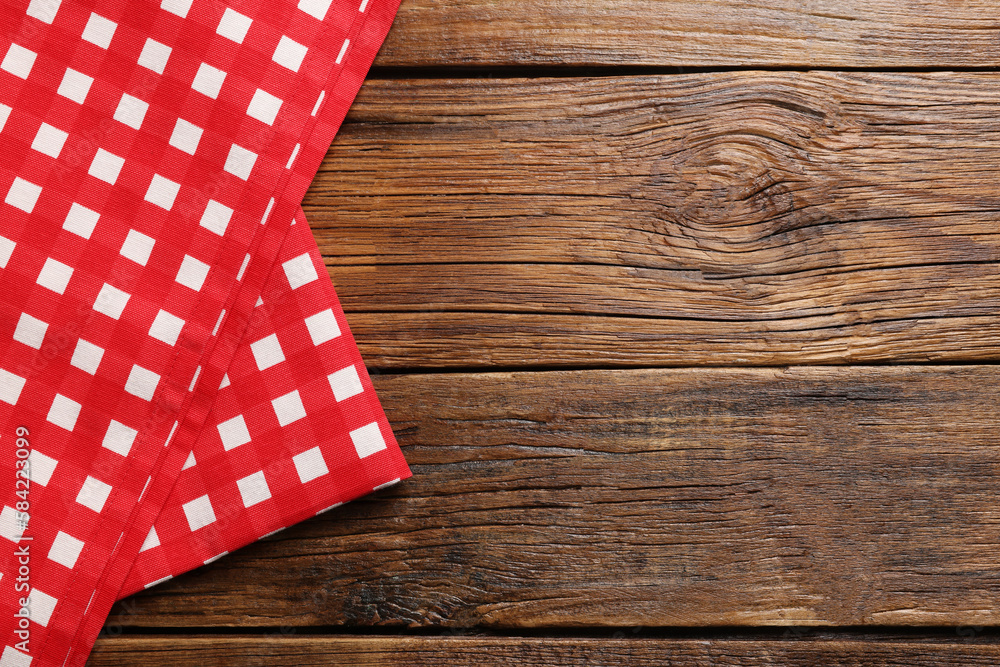 Obraz premium Red checkered tablecloth on wooden table, top view. Space for text