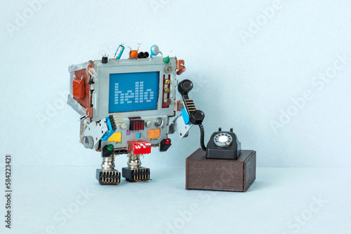 A toy robot retro computer holds a handset of an old vintage rotary phone. The concept of analog voice communication between telephone subscribers