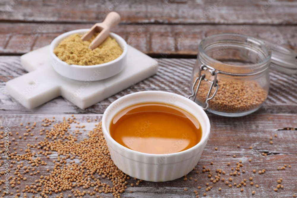 Bowl of natural oil, mustard seeds and powder on wooden table Bowl of natural oil, mustard seeds and powder on wooden table
