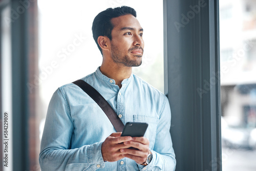 Phone, thinking and man by office window for career inspiration, job search  or online networking. Contemplating asian person or young entrepreneur  cellphone, smartphone or mobile app in workplace Stock Photo