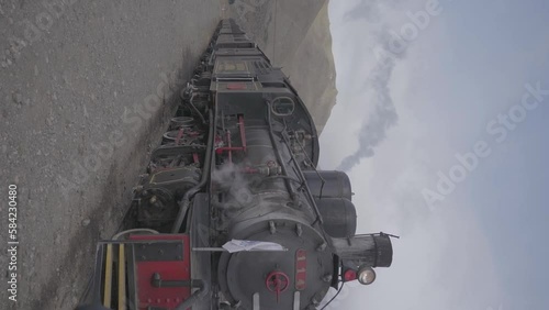 A vintage steam engine locamotive in Patagonia, Argentina with mountains in the background. A slow motion vertical shot of a train with the Argentinian flag flying in the wind. photo