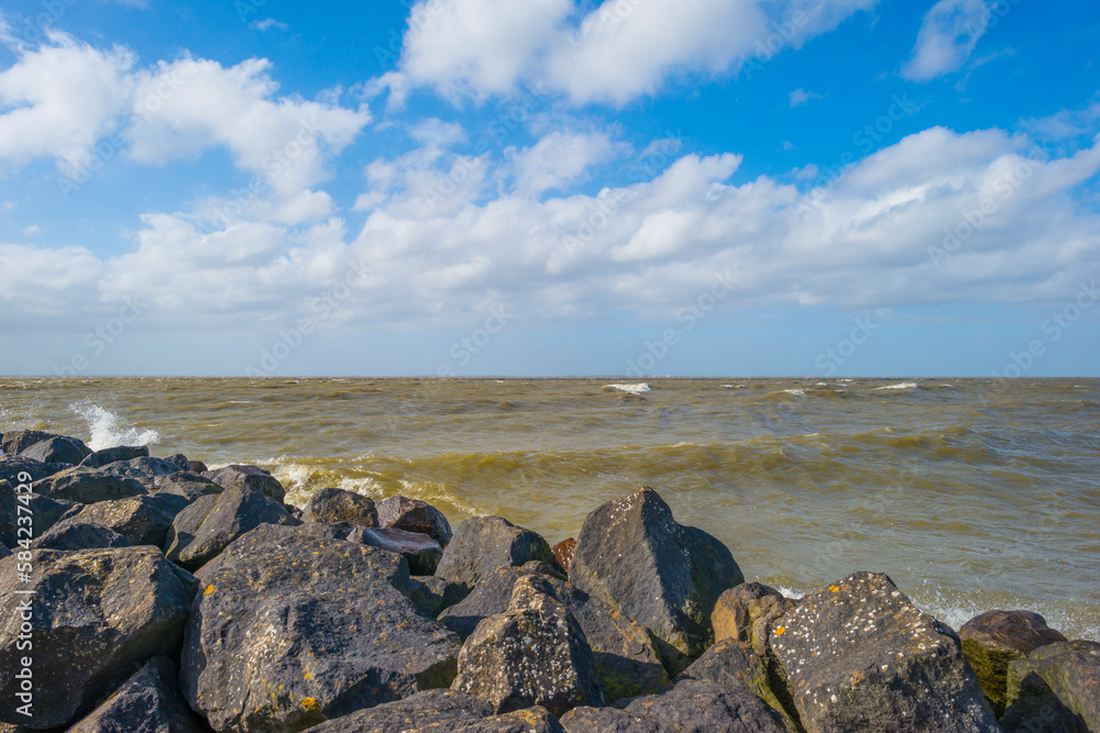 Dike along a stormy lake below a blue sky and white clouds in winter, Markerwaard, Almere, Flevoland, The Netherlands, March 13, 2023
