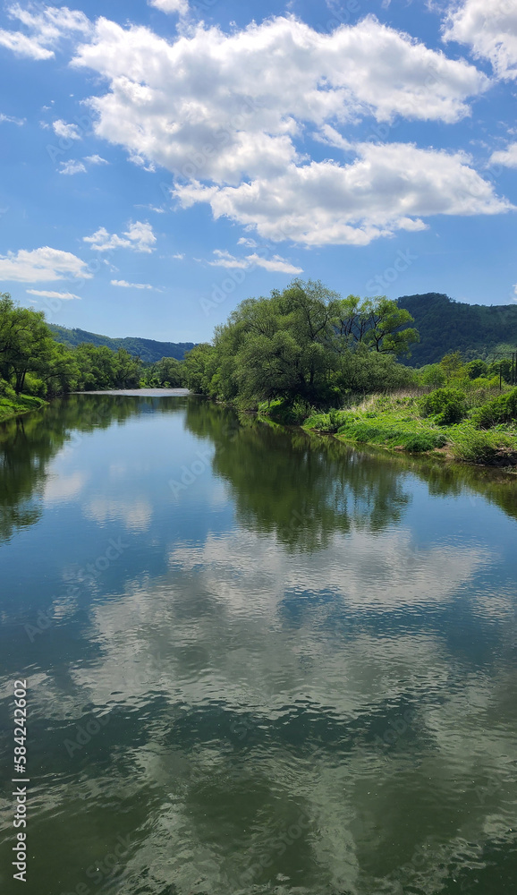 River Uzh near the village of Perechyn, reflection of clouds in the water, spring sunny day in the Carpathians of the Transcarpathian region of Ukraine