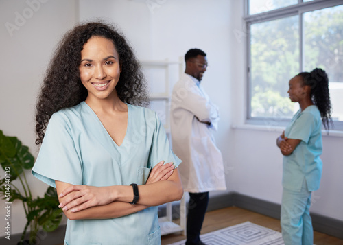Portrait of nurse with curly hair arms folded, smiling - with team in background photo