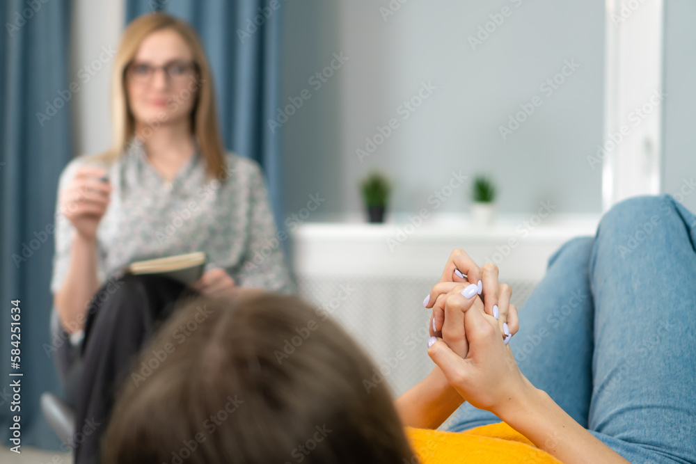 Naklejka premium Focus on the hands of a patient lying on the couch at a psychologist's appointment. Woman is being consulted by a psychotherapist. Psychology, psychosomatics, coach