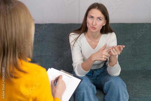 Woman consults with colleague writes important theses into tablet on paper. Journalist takes interview sitting on chair at home. View from back. Communication of two beautiful girls. photo