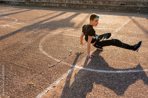 Valokuva Teenage boy with blue hair breakdancing on a basketball court in the street