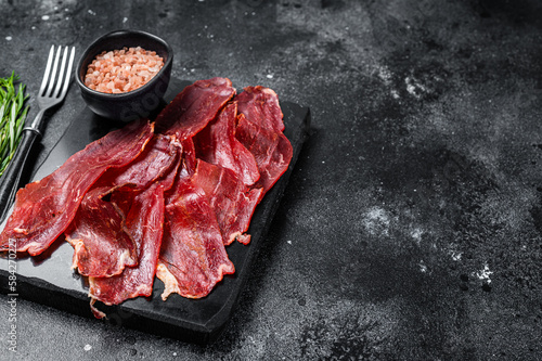 Turkish sliced pastrami (kayseri pastirma), dried beef meat with spices on marble board. Black background. Top view. Copy space