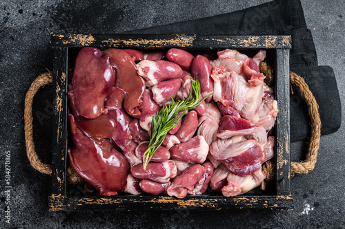 Uncooked Bird offals, raw chicken giblets, gizzards, stomachs, liver and hearts in a wooden tray. Black background. Top view