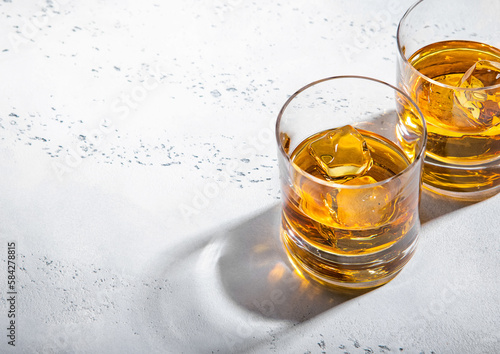 Two whiskey glasses with ice cubes on light background.